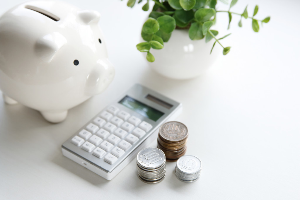 white piggy bank along with a calculator and coins off different amount on a desk