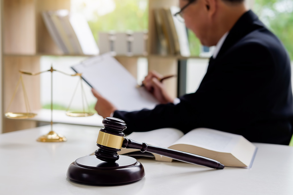 Judge reading business regulations with a law book and gavel on table.