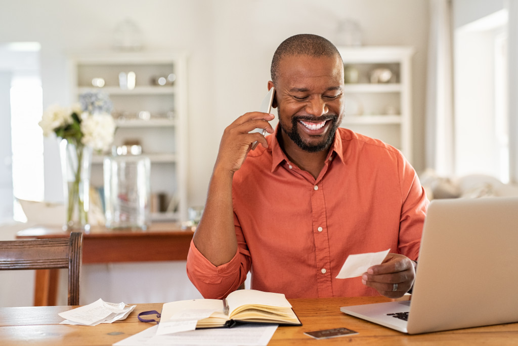 Happy mature man looking at invoice while talking on phone with bank