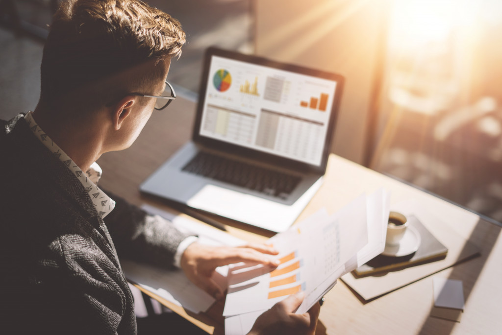 businessman with glasses reviewing charts in his document and in the laptop